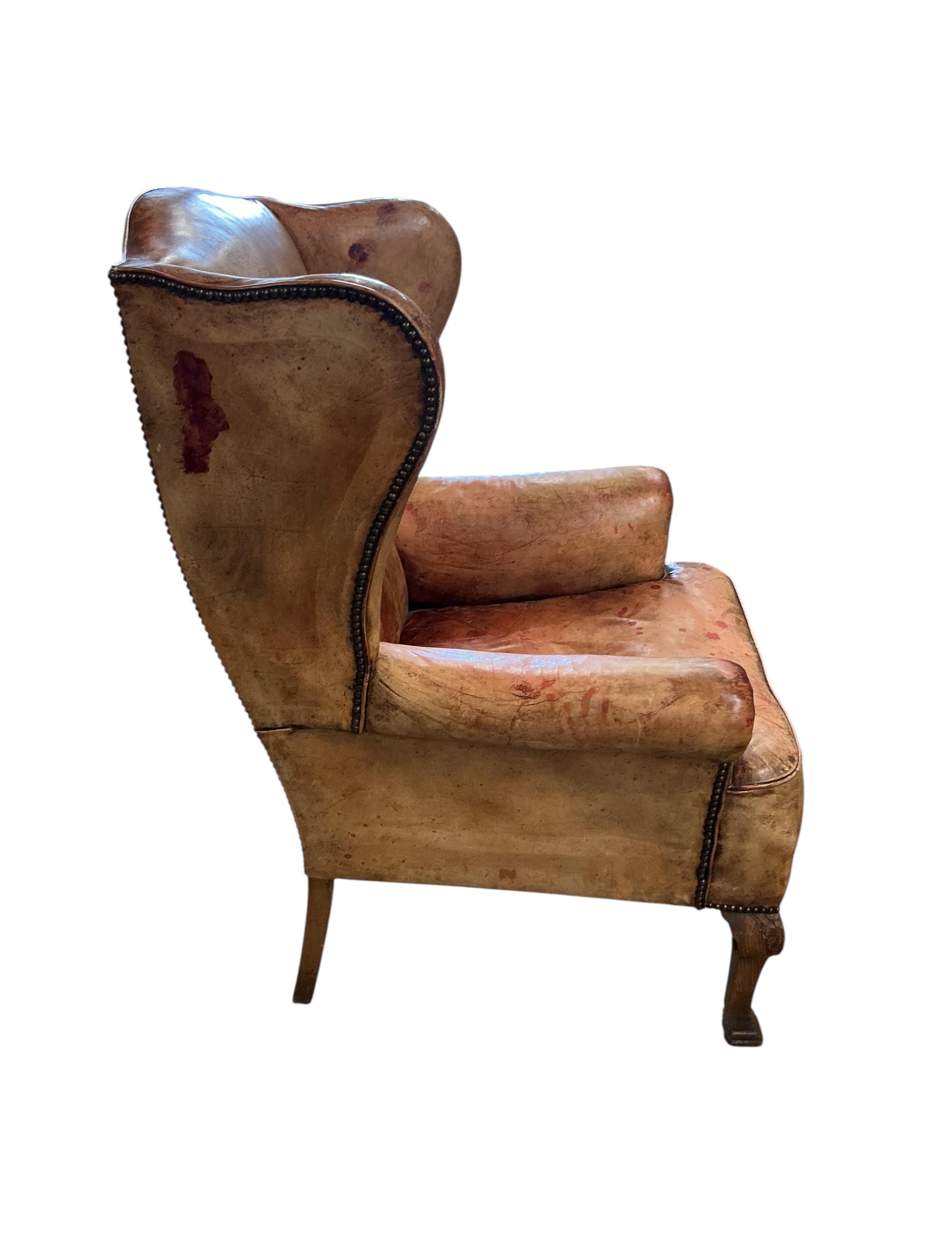 A George III style studded pale red leather wing armchair on carved oak cabriole legs, width 74cm, depth 78cm, height 110cm